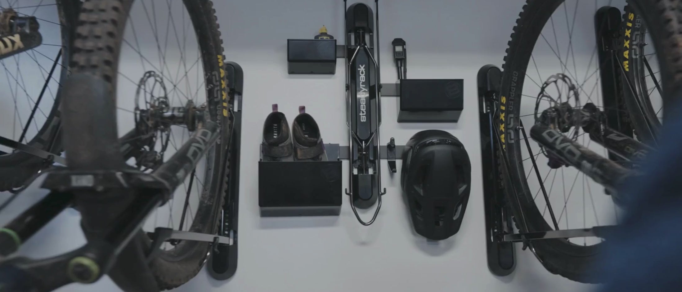 A person taking a helmet off a black hook connected to a wall mounted bike rack. 